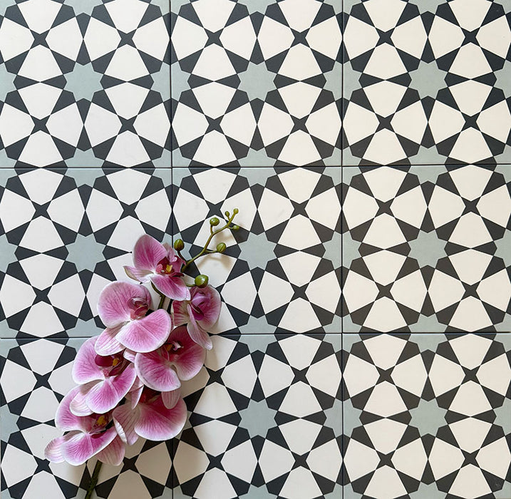 Agadir Blau Fliesen im marokkanischen Stil im Format 20 × 20 cm aus Feinsteinzeug, verlegt in einem sich wiederholenden geometrischen Sternmuster in Blau, Schwarz und Weiß. Mit einer dekorativen Orchidee in Szene gesetzt, um das detailreiche Design hervorzuheben.