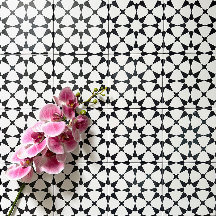 Agadir MINI Schwarz & Weiß Fliesen im marokkanischen Stil im Format 15 × 15 cm aus Feinsteinzeug, verlegt in einem sich wiederholenden geometrischen Sternmuster. Mit einer dekorativen Orchidee in Szene gesetzt, um den starken Schwarz-Weiß-Kontrast hervorzuheben.