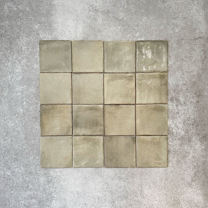 Flatlay von Zellige Waldgrün Matt Keramik-Quadratfliesen im marokkanischen Stil im Format 10 × 10 cm, das die sanfte grüne Farbvariation, die unregelmäßigen Kanten und die handgefertigte Glasuroptik auf neutralem Hintergrund hervorhebt.