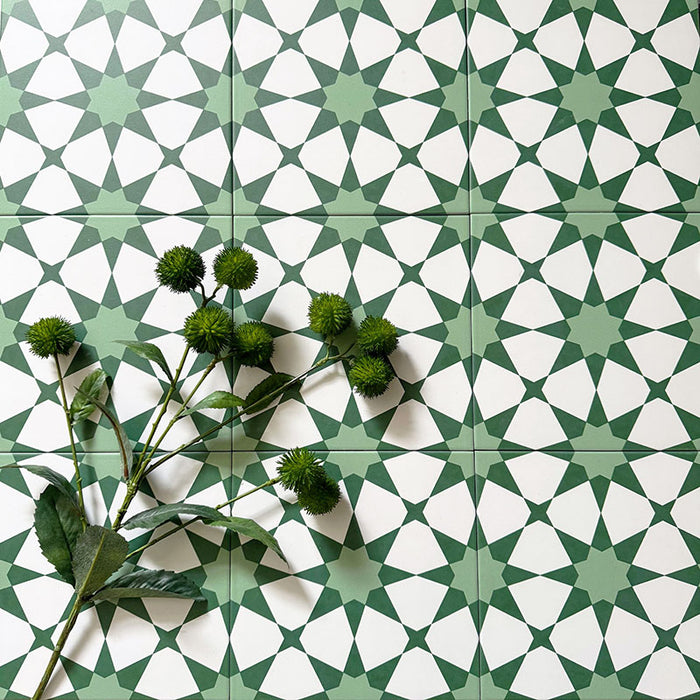 Marketingmotiv mit Agadir Grün Fliesen im marokkanischen Stil im Format 20 × 20 cm aus Feinsteinzeug, verlegt in einem sich wiederholenden geometrischen Sternmuster in sanftem Grün und Weiß. Mit Pflanzen dekoriert, um das frische, dekorative Design zu betonen.