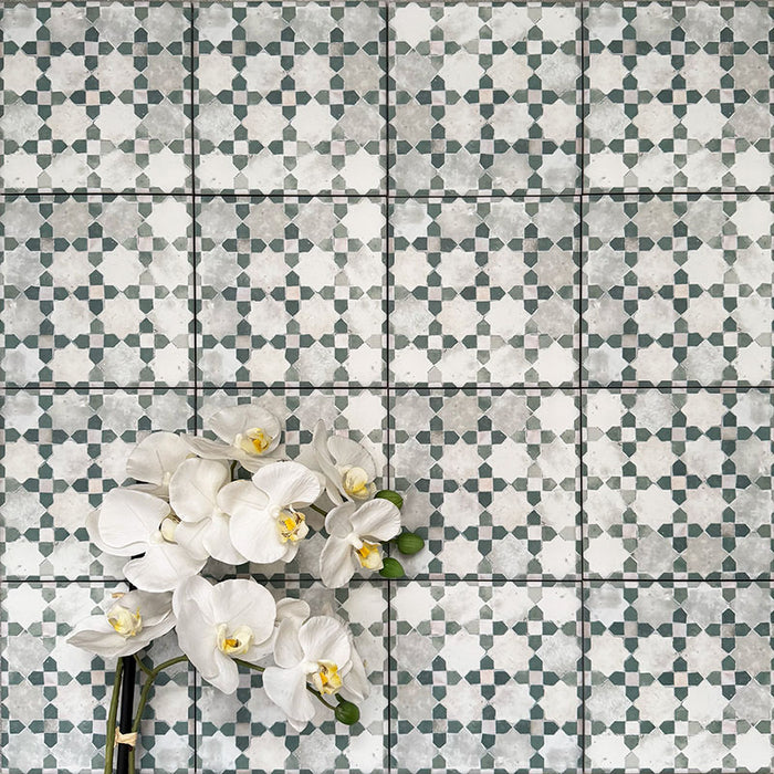 Berber Mequinez Grün Feinsteinzeugfliesen im marokkanischen Stil im Format 15 × 15 cm, verlegt im Raster, um das weiche geometrische Design in Grün und Creme zu zeigen. Mit floraler Dekoration in Szene gesetzt für eine wohnliche, dekorative Wirkung.