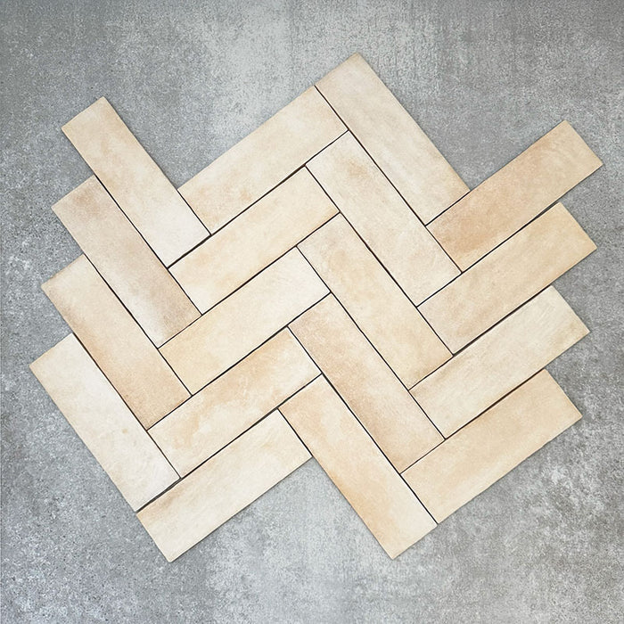 Flatlay von Zellige Sandbeige Matt Ziegel Keramikfliesen im marokkanischen Stil im Format 6,5 × 20 cm, in warmen Beige- und Cremetönen. Im Fischgrätmuster arrangiert, mit feiner Farbvariation und sanft unregelmäßigen Kanten auf strukturiertem grauem Hintergrund, um den authentischen Zellige-Effekt zu zeigen.