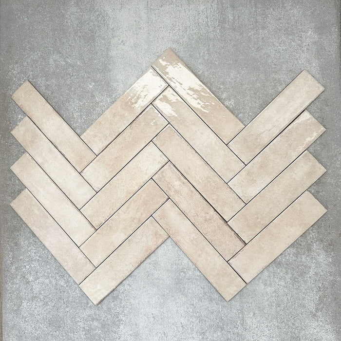 Nomadin Brick Creme Wandfliesen im Format 6 × 24,6 cm, im Fischgrätmuster verlegt, um den warmen, neutralen Farbton, die glänzende Oberfläche und die feine Oberflächenvariation hervorzuheben.