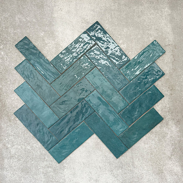 Flatlay von Zellige Pfauengrün Keramik-Ziegelfliesen im marokkanischen Stil im Format 6,5 × 20 cm, im Fischgrätmuster angeordnet. Die tiefen Blau-Grün-Töne, die glänzende Glasur in handgefertigter Optik und die natürliche Farbvariation kommen so besonders gut zur Geltung.