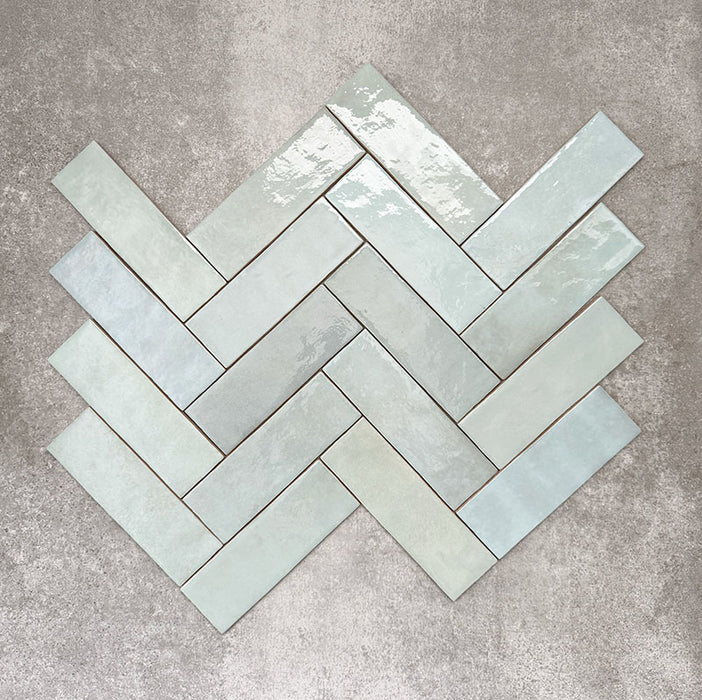 Flatlay von Zellige Aquablau Keramik-Riemchenfliesen im marokkanischen Stil im Format 6,5 × 20 cm, im Fischgrätmuster arrangiert. Die sanften Blau-Grün-Töne, die glänzende Glasur und die feine tonale Variation kommen dabei besonders zur Geltung.