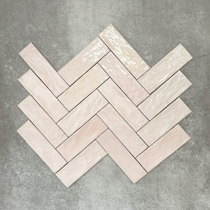 Flatlay von Zellige Rosa Nebel Ziegel Keramikfliesen im marokkanischen Stil im Format 6,5 × 20 cm, in sanften Rosa- und Blushtönen. Im Fischgrätmuster auf strukturiertem grauem Hintergrund angeordnet, um die glänzende Glasur, die feine Farbvariation und den handwerklichen Zellige-Effekt zu zeigen.