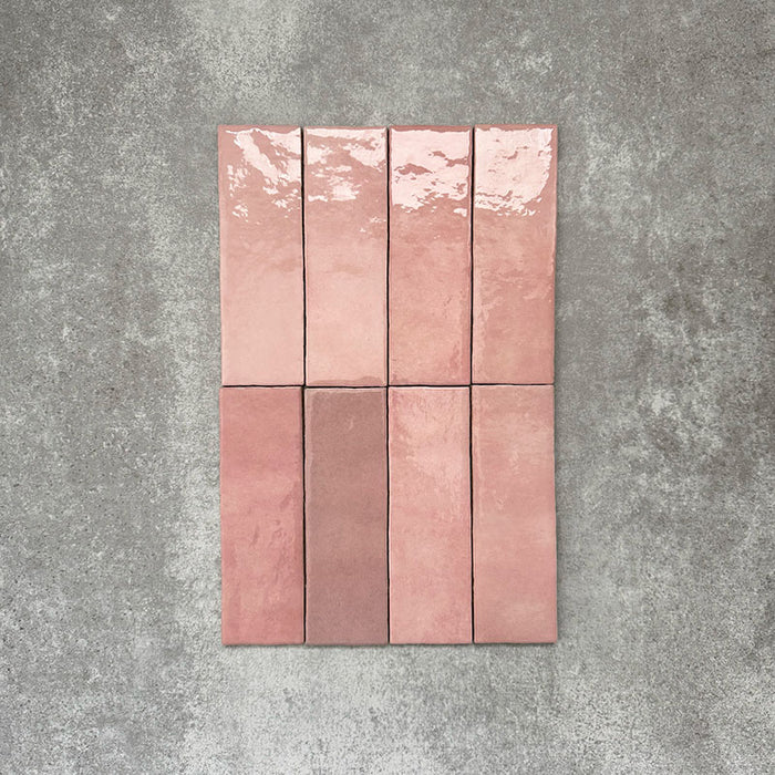 Flatlay von Zellige Rosa Brick Keramikfliesen im marokkanischen Stil im Format 6,5 × 20 cm, gezeigt in sanften Blush-, Altrosa- und Terrakotta-Pinktönen mit feiner tonaler Variation und leicht unregelmäßigen Kanten. Vertikal im Ziegelverband auf strukturiertem grauem Hintergrund arrangiert, um die handwerkliche Zellige-Glasur hervorzuheben.