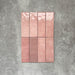 Flatlay von Zellige Rosa Brick Keramikfliesen im marokkanischen Stil im Format 6,5 × 20 cm, gezeigt in sanften Blush-, Altrosa- und Terrakotta-Pinktönen mit feiner tonaler Variation und leicht unregelmäßigen Kanten. Vertikal im Ziegelverband auf strukturiertem grauem Hintergrund arrangiert, um die handwerkliche Zellige-Glasur hervorzuheben.