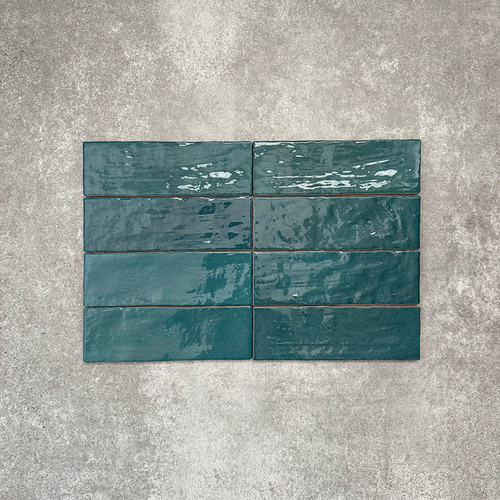 Flatlay von Zellige Pfauengrün Keramik-Ziegelfliesen im marokkanischen Stil im Format 6,5 × 20 cm, mit satten Blau-Grün-Tönen, glänzender Glasur und natürlicher Farbvariation auf neutralem Hintergrund.