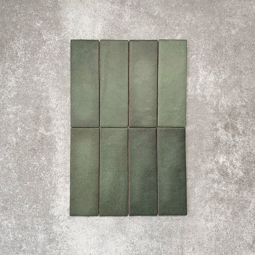 Flatlay von Zellige Malachitgrün Matt Keramik-Riemchenfliesen im marokkanischen Stil im Format 6,5 × 20 cm, das die feine tonale Variation, die handwerkliche Oberflächenstruktur und den satten Grünton vor neutralem Hintergrund zeigt.