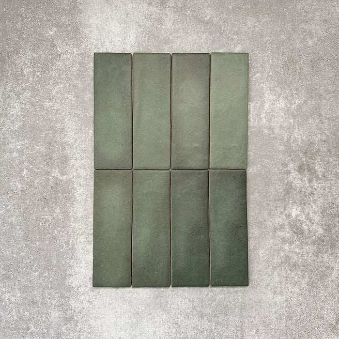 Flatlay von Zellige Malachitgrün Matt Keramik-Riemchenfliesen im marokkanischen Stil im Format 6,5 × 20 cm, das die feine tonale Variation, die handwerkliche Oberflächenstruktur und den satten Grünton vor neutralem Hintergrund zeigt.