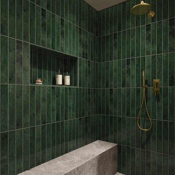 Begehbare Dusche mit Malediven Grün Wandfliesen im Format 5 × 40 cm aus glänzender Keramik, vertikal verlegt mit intensiver grüner Tonvariation. Kombiniert mit Messingarmaturen, einer integrierten Nische und einer Sitzbank in Marmoroptik für eine hochwertige, ruhige Gesamtwirkung.