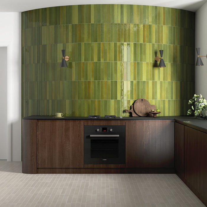 Moderne Küche mit Lisbon Olive Green Wandfliesen aus Feinsteinzeug im handwerklichen Stil im Format 5 × 30 cm, vertikal auf einer geschwungenen Akzentwand verlegt. Kombiniert mit dunklen Holzfronten und schwarzen Arbeitsplatten entsteht ein ausdrucksstarkes, von der Natur inspiriertes Interior.