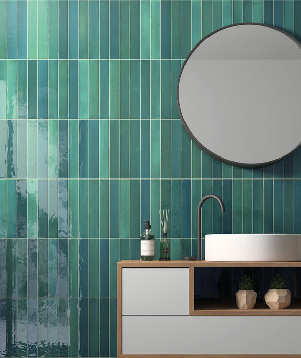 Modernes Badezimmer mit Lisbon Verde Green Wandfliesen aus Feinsteinzeug im handwerklichen Stil im Format 5 × 30 cm, vertikal verlegt, um eine markante Akzentwand zu schaffen. Kombiniert mit einem schwebenden Waschtischunterschrank, schwarzen Armaturen und einem runden Spiegel entsteht ein modernes, von der Natur inspiriertes Interior.