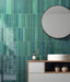 Modernes Badezimmer mit Lisbon Verde Green Wandfliesen aus Feinsteinzeug im handwerklichen Stil im Format 5 × 30 cm, vertikal verlegt, um eine markante Akzentwand zu schaffen. Kombiniert mit einem schwebenden Waschtischunterschrank, schwarzen Armaturen und einem runden Spiegel entsteht ein modernes, von der Natur inspiriertes Interior.