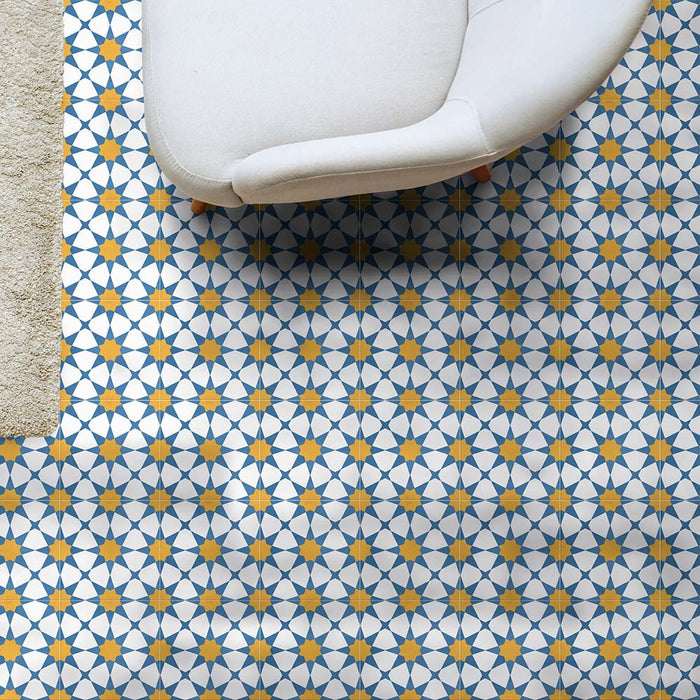 Wohnzimmergestaltung mit Agadir Blau & Gelb Fliesen im marokkanischen Stil im Format 20 × 20 cm aus Feinsteinzeug, verlegt als Bodenbelag mit geometrischem Sternmuster in Blau, Weiß und warmem Gelb. In Kombination mit einem modernen Sofa entsteht eine helle, einladende Raumwirkung.