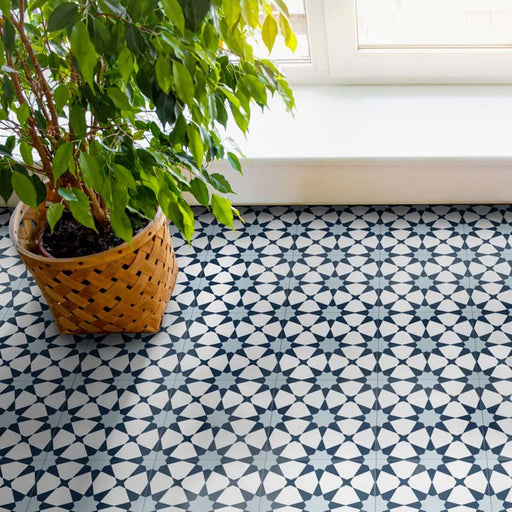 Wohnbereich mit Agadir Blau Fliesen im marokkanischen Stil im Format 20 × 20 cm aus Feinsteinzeug, verlegt als Bodenbelag mit geometrischem Sternmuster in Blau und Weiß. Natürliches Licht und eine Zimmerpflanze sorgen für eine frische, moderne Raumwirkung.