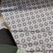 Marketingmotiv mit Agadir Beige Fliesen im marokkanischen Stil im Format 20 × 20 cm aus Feinsteinzeug, verlegt als Bodenbelag mit einem sanften, neutralen geometrischen Sternmuster in dezenten Grau- und warmen Beigetönen. Mit einem Holzstuhl in Szene gesetzt, um eine wohnliche, authentische Atmosphäre zu vermitteln.
