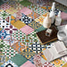 Fayrouz Mini Patchwork Feinsteinzeugfliesen im marokkanischen Stil im Format 15 × 15 cm, verlegt in einem lebendigen Patchwork-Muster. Der eklektische Mix aus geometrischen und floralen Motiven in zarten Rosatönen, Salbeigrün, tiefem Blau, Senfgelb, Terrakotta und neutralen Nuancen wird mit dekorativen Accessoires kombiniert und schafft eine warme, charaktervolle Wohnatmosphäre.