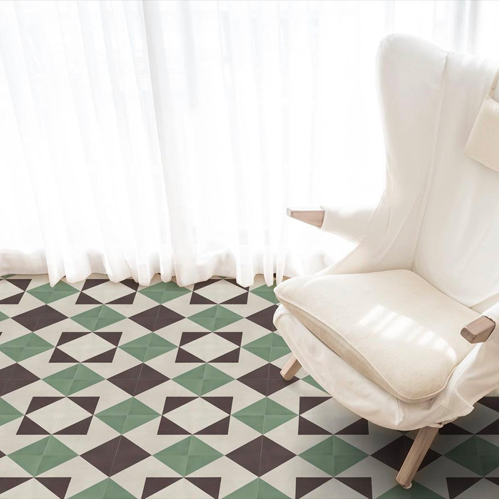 Wohnzimmerinterieur mit Abstrakte Winkel Musterfliese im Format 20 × 20 cm, verlegt als geometrisches Bodendesign. Das sich wiederholende, kantige Muster in gedecktem Grün, tiefem Anthrazit und sanften Cremetönen sorgt für eine klare, zeitgemäße Optik und wird mit einem weißen Sessel und leichten, transparenten Vorhängen für ein helles, modernes Ambiente in Szene gesetzt.