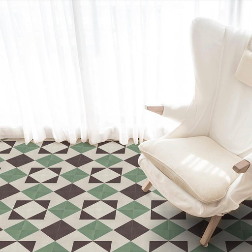Wohnzimmerinterieur mit Abstrakte Winkel Musterfliese im Format 20 × 20 cm, verlegt als geometrisches Bodendesign. Das sich wiederholende, kantige Muster in gedecktem Grün, tiefem Anthrazit und sanften Cremetönen sorgt für eine klare, zeitgemäße Optik und wird mit einem weißen Sessel und leichten, transparenten Vorhängen für ein helles, modernes Ambiente in Szene gesetzt.
