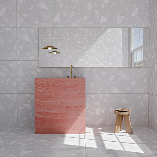 Badezimmer mit Melodie Rock Terrazzo Weiß Wand- und Bodenfliesen im Format 60 × 120 cm mit großformatiger Terrazzo-Optik, kombiniert mit einem auffälligen rosafarbenen Waschtischunterschrank, Messingarmaturen und warmen Holzdetails.