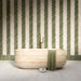 Modernes Badezimmer mit Nomadin Brick Creme Wandfliesen im Industriestil im Format 6 × 24,6 cm, im markanten Fischgrätmuster verlegt. Kombiniert mit salbeigrünen Akzenten, einer freistehenden Badewanne in Steinoptik und Armaturen in gebürsteter Messingoptik entsteht ein stilvolles und modernes Interior.