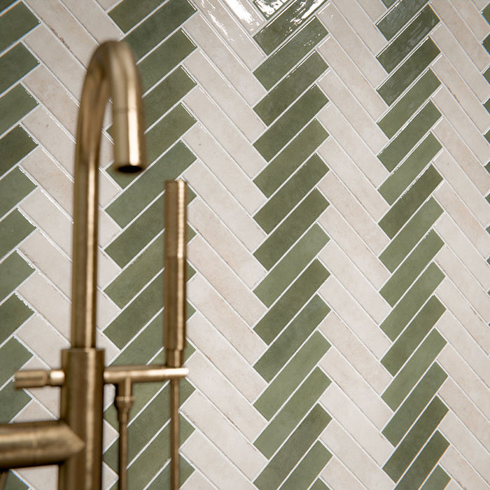 Modernes Badezimmer mit Nomadin Brick Creme Wandfliesen im Industriestil im Format 6 × 24,6 cm, im markanten Fischgrätmuster verlegt. Kombiniert mit salbeigrünen Akzenten, einer freistehenden Badewanne in Steinoptik und Armaturen in gebürsteter Messingoptik entsteht ein stilvolles und modernes Interior.