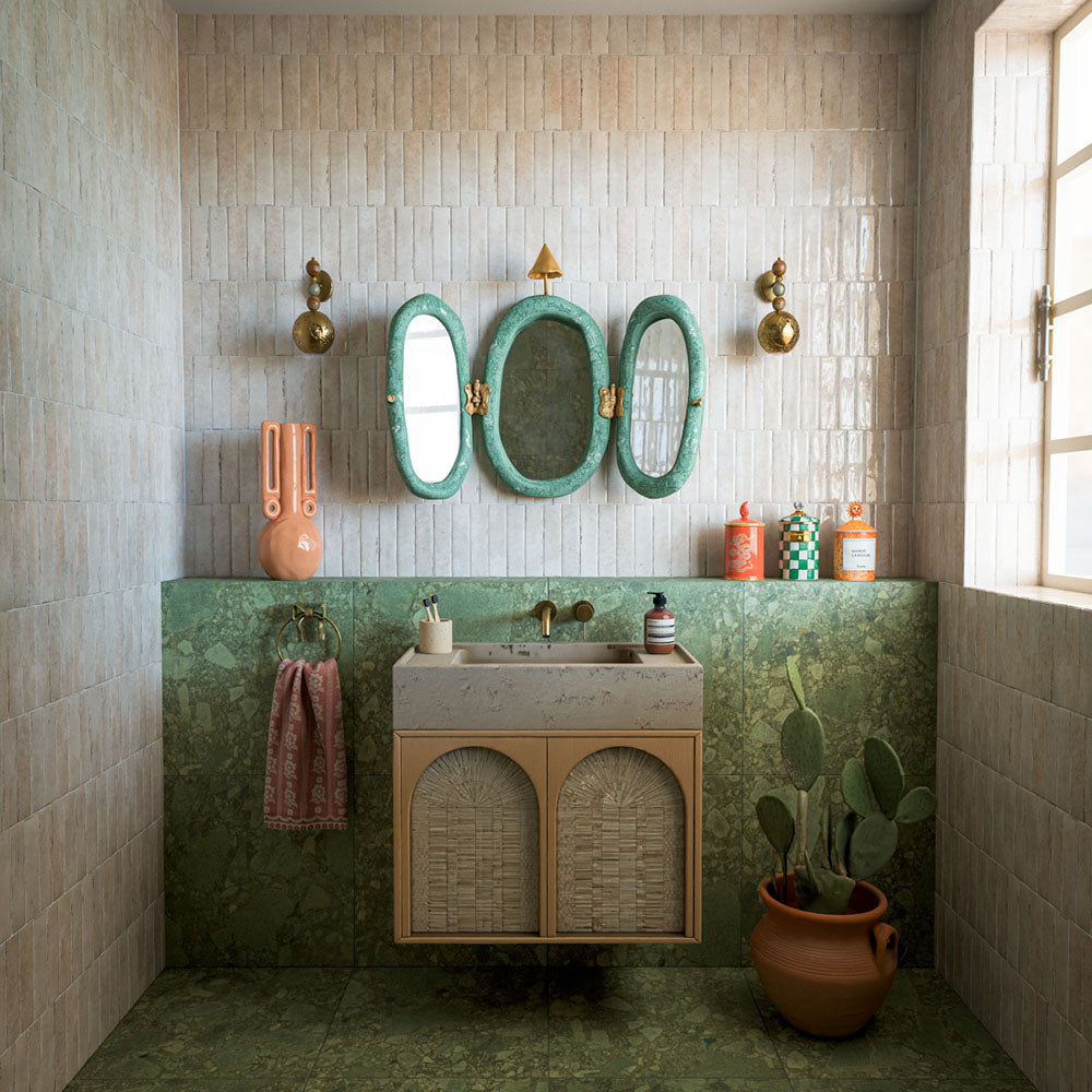 Badezimmer mit Nomadin Brick Creme Wandfliesen im Industriestil im Format 6 × 24,6 cm, kombiniert mit Oberflächen in grüner Marmoroptik, einem schwebenden Waschtischunterschrank, dekorativen Spiegeln und warmen Akzenten in Messingoptik für einen modernen Look.