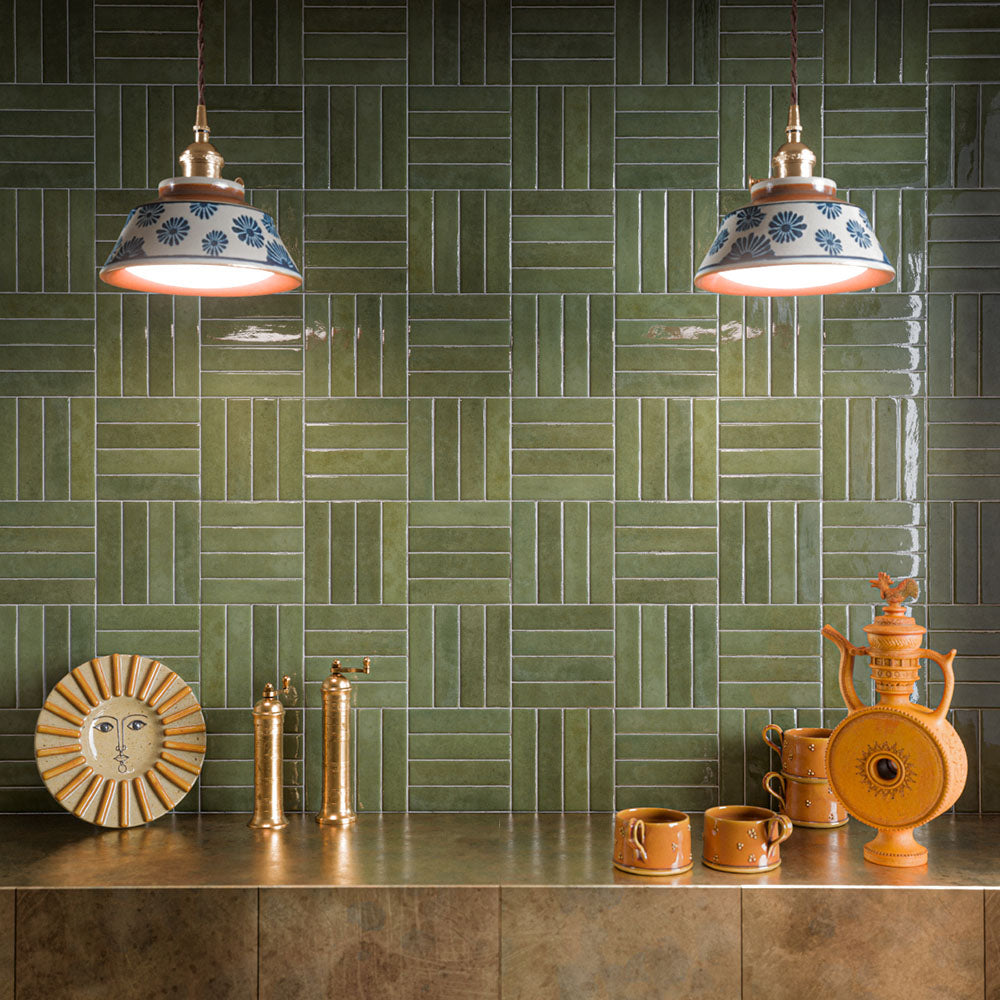 Moderne Küchenrückwand mit Nomadin Salbeigrün glänzenden Brick-Wandfliesen, im Korbflechtmuster verlegt, kombiniert mit bronzefarbenen Arbeitsplatten, Armaturen in Messingoptik, keramischen Pendelleuchten und warmen Terrakotta-Accessoires für ein ausdrucksstarkes Interior voller Charakter.