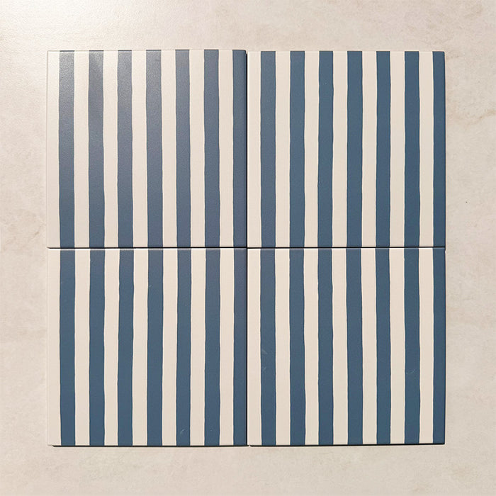 Produktpräsentation der Gestreift Blau Dekorfliesen im Format 20 × 20 cm in sanften Blau- und Weißtönen, mit unregelmäßigen vertikalen Streifen in handgemalter Optik vor einem Hintergrund in dezenter Steinoptik.