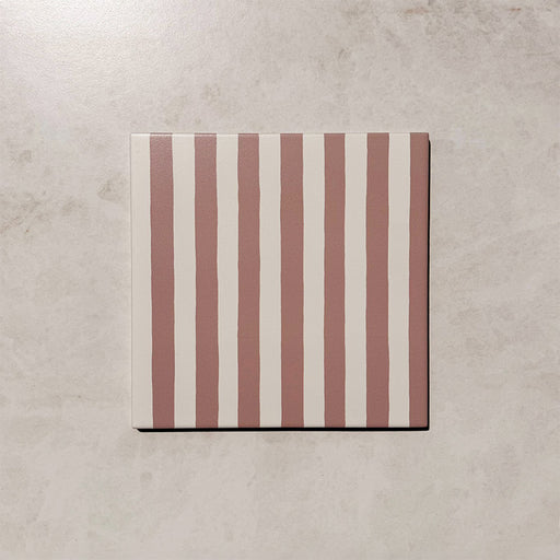 Produktpräsentation der Gestreift Rosa Dekorfliesen im Format 20 × 20 cm in sanften Blush- und Weißtönen, mit unregelmäßigen vertikalen Streifen in handgemalter Optik vor einem Hintergrund in dezenter Steinoptik.