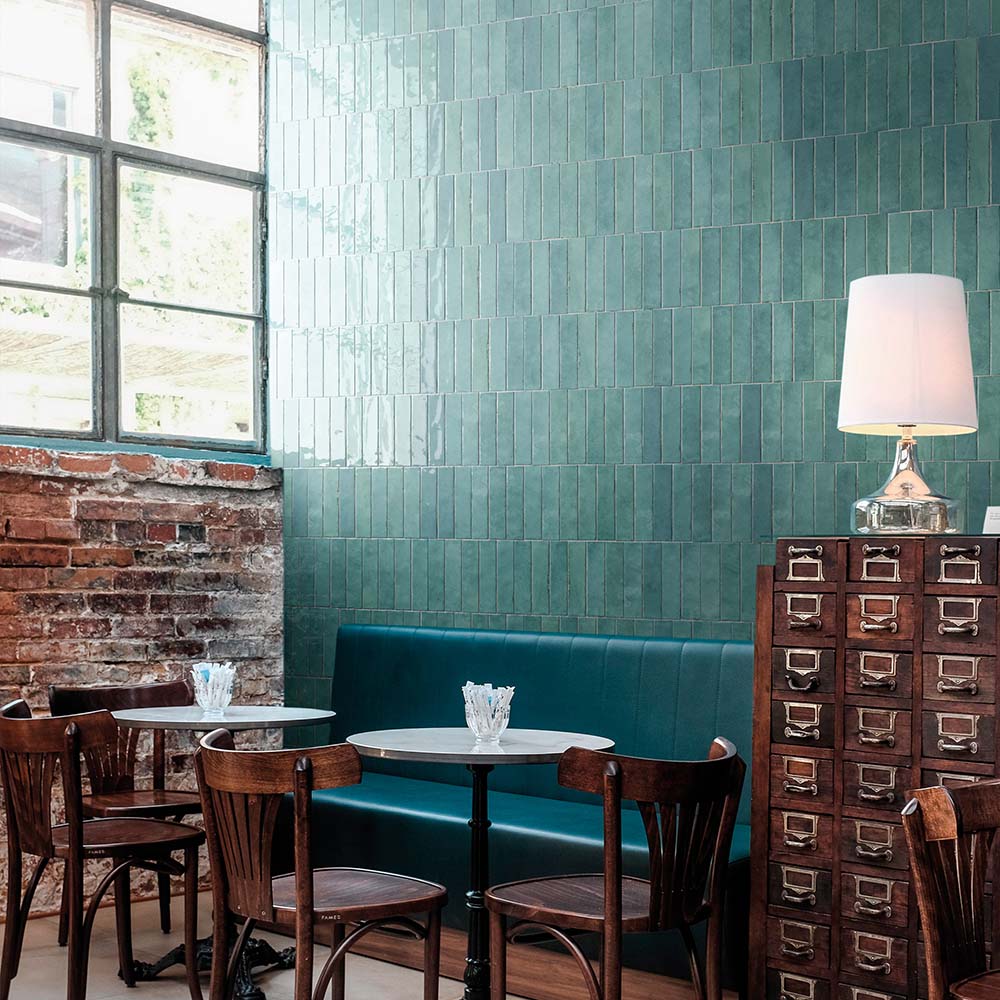 Restaurantinterieur mit Nomadin Aqua Ziegel-Wandfliesen im Format 6 × 24,6 cm, vertikal verlegt, um eine satte petrolfarbene Akzentwand mit industriellem Charakter zu schaffen.