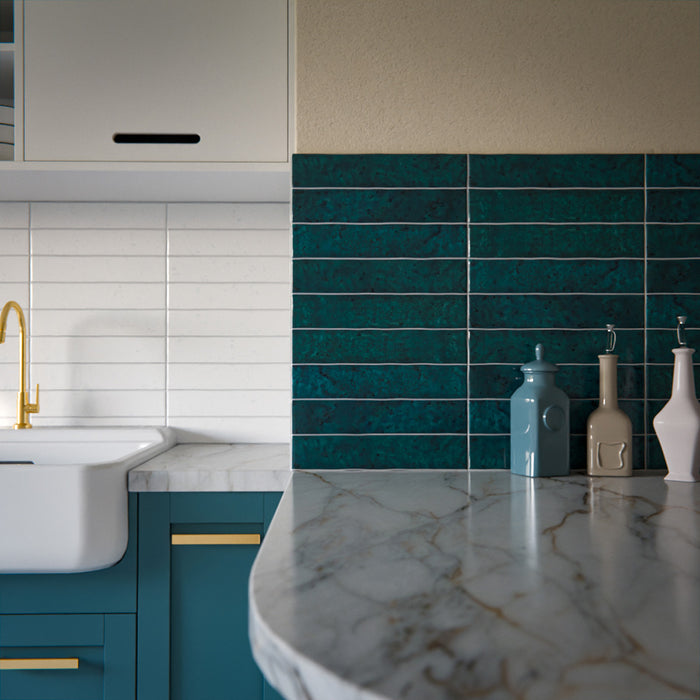 Küchenrückwand mit Bora Bora Ziegel Amun Blau Keramik-Wandfliesen im schlanken Riemchenformat 6,5 × 32,8 cm mit Fluxglasur, horizontal verlegt, um die satte Blau-Grün-Tonvariation zu betonen. In Kombination mit petrolfarbenen Schrankfronten, Arbeitsplatten in Marmoroptik und Armaturen in Messing entsteht ein ausdrucksstarker, zeitgemäßer Look.