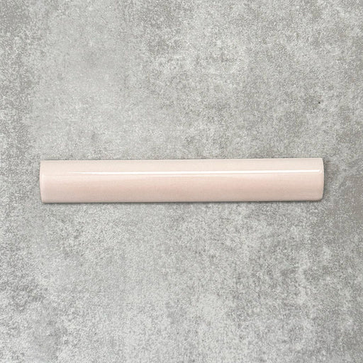 Flatlay mit Zellige Rosa Nebel Bullnose Keramik-Abschlussfliesen im marokkanischen Stil im Format 3 × 20 cm, in sanften, hellen Rosétönen. Die glatte, abgerundete Kante und die glänzende Glasur werden auf einem strukturierten grauen Hintergrund präsentiert, um den handwerklichen Zellige-Effekt und das dekorative Kantenprofil zu betonen.