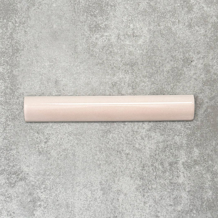 Flatlay mit Zellige Rosa Nebel Bullnose Keramik-Abschlussfliesen im marokkanischen Stil im Format 3 × 20 cm, in sanften, hellen Rosétönen. Die glatte, abgerundete Kante und die glänzende Glasur werden auf einem strukturierten grauen Hintergrund präsentiert, um den handwerklichen Zellige-Effekt und das dekorative Kantenprofil zu betonen.