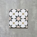 Einzelne Agadir Beige Fliese im marokkanischen Stil im Format 20 × 20 cm aus Feinsteinzeug mit einem zurückhaltenden geometrischen Sternmuster in Weiß, ergänzt durch gedeckte Beige-, Oliv- und Anthrazitakzente auf einer leicht strukturierten Oberfläche.