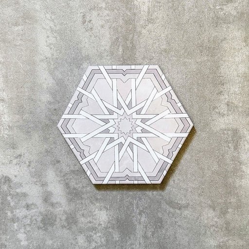 Einzelne Medina Hormuz Schneeweiß Feinsteinzeug-Hexagonfliese im marokkanischen Stil im Format 18,7 × 21,6 cm, mit einem präzisen, sterninspirierten geometrischen Muster in Weiß- und sanften Grautönen, gezeigt vor neutralem Hintergrund.