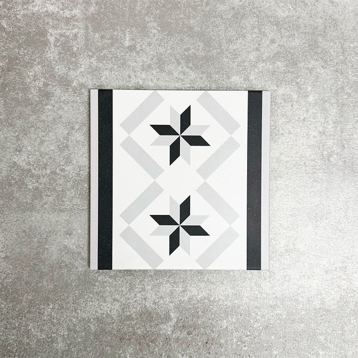 Einzelne Canterbury Stern Feinsteinzeug-Bordürenfliese im viktorianischen Stil im Format 20 × 20 cm mit einem sich wiederholenden Sternmotiv, eingefasst von kontrastierenden schwarzen und grauen Streifen. Auf neutralem Hintergrund dargestellt, um die Verwendung als dekorative Bordüre für Wand- und Bodenverlegungen hervorzuheben.