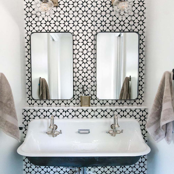 Waschbereich im Badezimmer mit Agadir MINI Schwarz & Weiß Fliesen im marokkanischen Stil im Format 15 × 15 cm aus Feinsteinzeug, verwendet als Wandfliesen mit auffälligem geometrischem Sternmuster. Kombiniert mit zwei Spiegeln, klassischem Waschbecken und verchromten Armaturen.