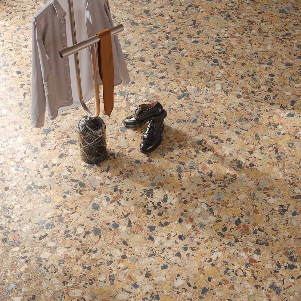 Overhead view of the Stuzzi Amber 60x120cm terrazzo style porcelain floor tiles, showcasing a warm amber base with multicoloured stone fragments in cream, ochre, rust, charcoal and grey. The realistic 4D brushed finish adds texture and depth, creating a striking terrazzo effect in a contemporary interior.