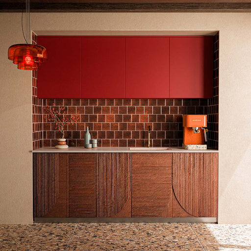 Küche mit Stuzzi Amber Bodenfliesen im Format 60 × 120 cm in klassischer Terrazzo-Optik mit gebürsteter 4D-Oberfläche, kombiniert mit sattroten Küchenschränken, strukturierten Holzpaneelen und dunkelbraunen Ziegelfliesen als Küchenrückwand.