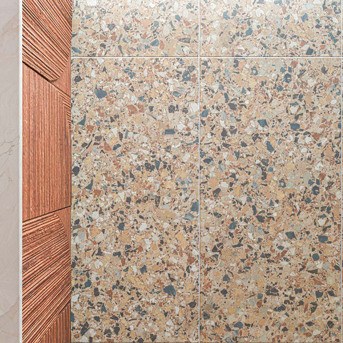 Nahaufnahme der Stuzzi Amber Bodenfliesen im Format 60 × 120 cm in klassischer Terrazzo-Optik mit gebürsteter 4D-Oberfläche, mit warmen bernsteinfarbenen, cremefarbenen und grauen Fragmenten in Steinoptik, neben strukturierten Küchenschränken aus Holz.