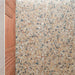 Nahaufnahme der Stuzzi Amber Bodenfliesen im Format 60 × 120 cm in klassischer Terrazzo-Optik mit gebürsteter 4D-Oberfläche, mit warmen bernsteinfarbenen, cremefarbenen und grauen Fragmenten in Steinoptik, neben strukturierten Küchenschränken aus Holz.
