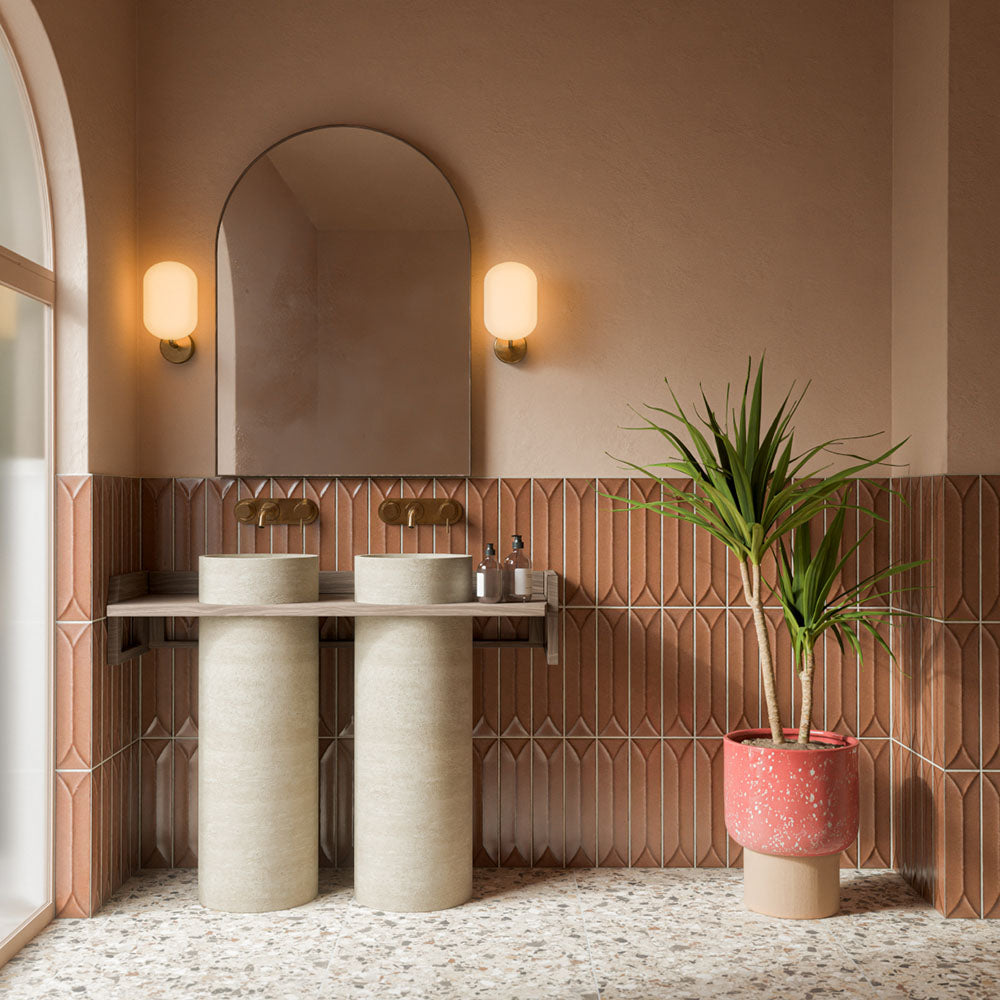Badezimmer mit Stuzzi Dolmia Bodenfliesen im Format 60 × 60 cm im klassischen Terrazzo-Stil mit gebürsteter 4D-Oberfläche, kombiniert mit terrakottafarbenen Akzentwänden, zwei Standwaschbecken, Messingarmaturen und grünen Pflanzen.