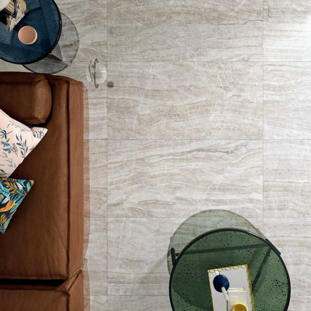 Living room featuring Taj Mahal Polished Marble effect 60 × 120cm porcelain floor tiles, styled with a leather sofa, glass side tables, and layered cushions, highlighting soft beige tones and natural flowing veining.