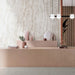 Interior setting featuring Taj Mahal Polished Marble effect 60 × 120cm porcelain wall and floor tiles, styled with a blush-toned counter, sculptural accessories, and soft lighting to highlight delicate veining and warm neutral tones.