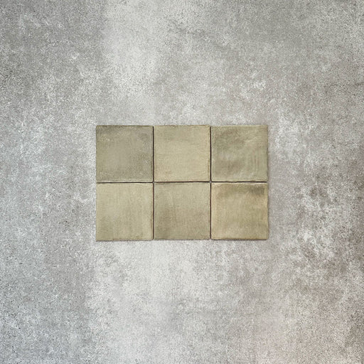 Flatlay von Zellige Waldgrün Matt Keramik-Quadratfliesen im marokkanischen Stil im Format 10 × 10 cm, mit weichen grünen und erdigen Tonabstufungen, leicht unregelmäßigen Kanten und handwerklicher Glasuroptik vor neutralem Hintergrund.