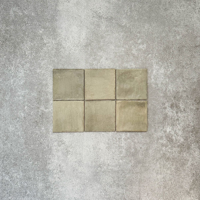 Flatlay von Zellige Waldgrün Matt Keramik-Quadratfliesen im marokkanischen Stil im Format 10 × 10 cm, mit weichen grünen und erdigen Tonabstufungen, leicht unregelmäßigen Kanten und handwerklicher Glasuroptik vor neutralem Hintergrund.