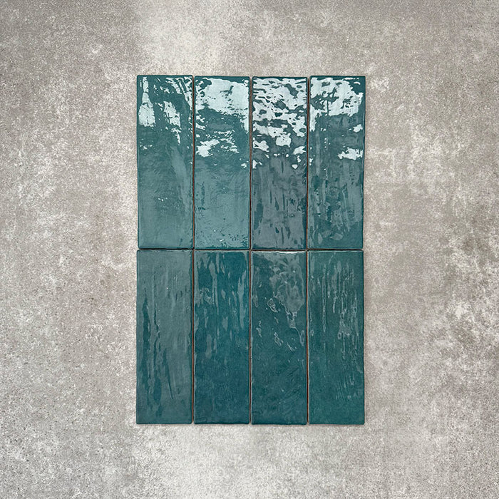 Flatlay von Zellige Pfauengrün Keramik-Ziegelfliesen im marokkanischen Stil im Format 6,5 × 20 cm, mit satten Blau-Grün-Tönen, glänzender Glasur in handgefertigter Optik und natürlicher Farbvariation auf neutralem Hintergrund.